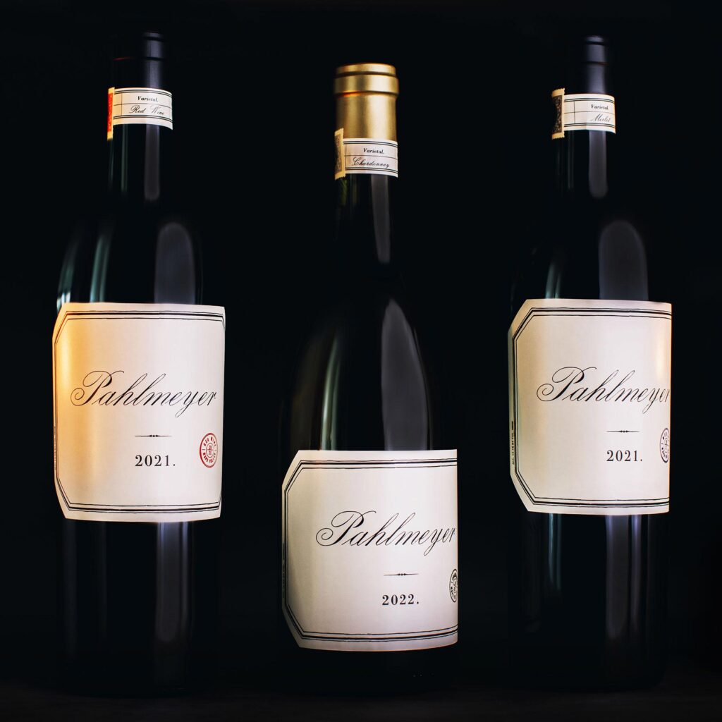 Three wine bottles with vintage labels: the left and right bottles are labeled “Pahlmeyer 2021,” and the center bottle is labeled “Pahlmeyer 2022,” all set against a black background.