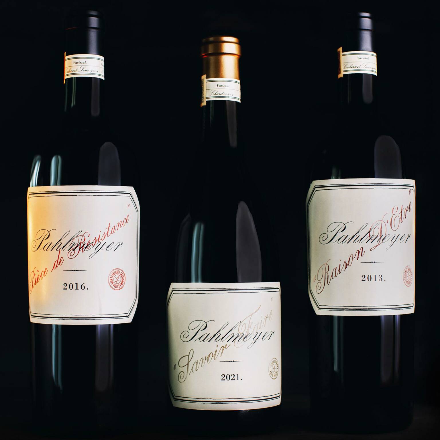 Three wine bottles are displayed against a dark background. The labels indicate vintages of 2016, 2021, and 2013. The central bottle has a slightly different label design from the others.