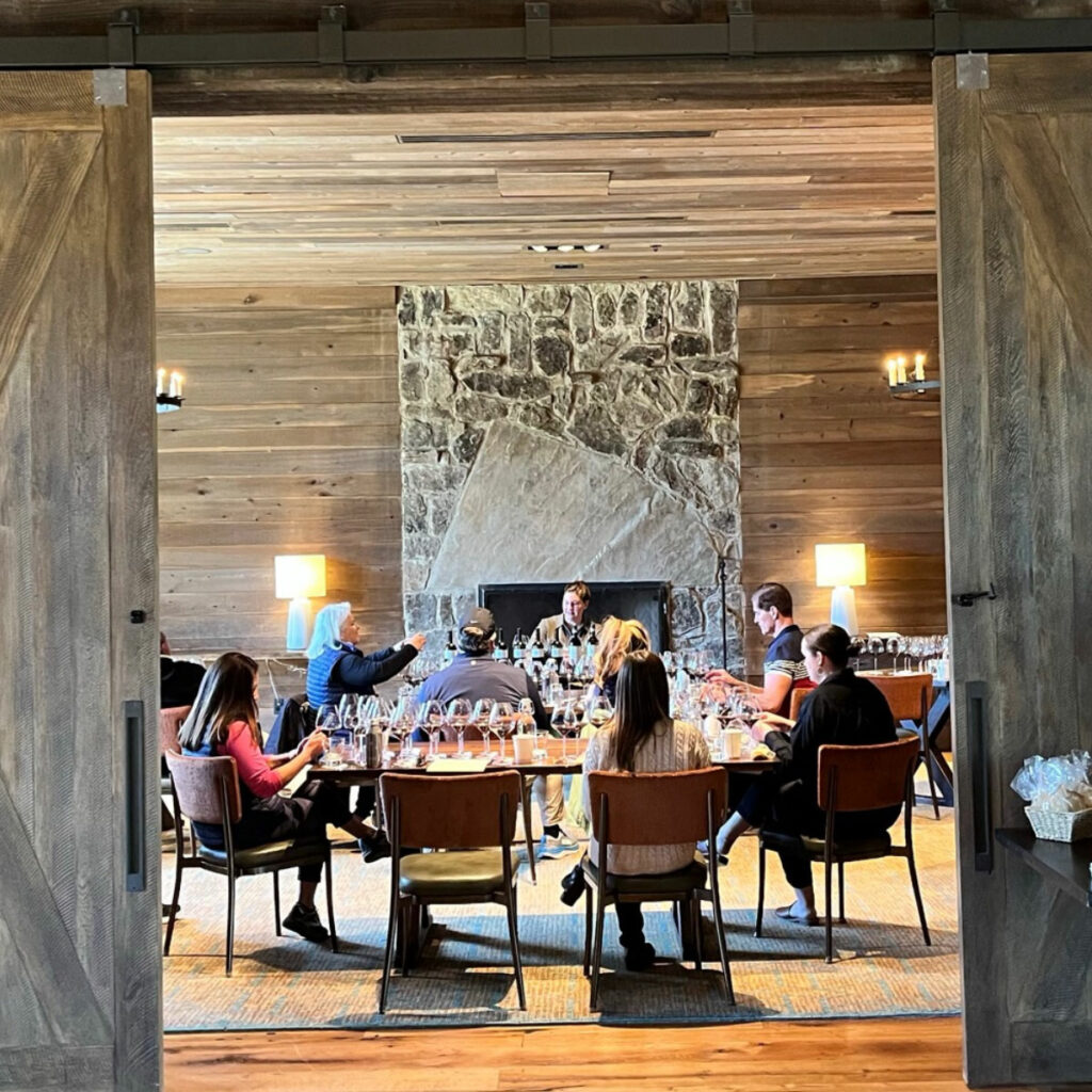 A group of people sit around a table in a wood-paneled room, engaging in a meeting or discussion.