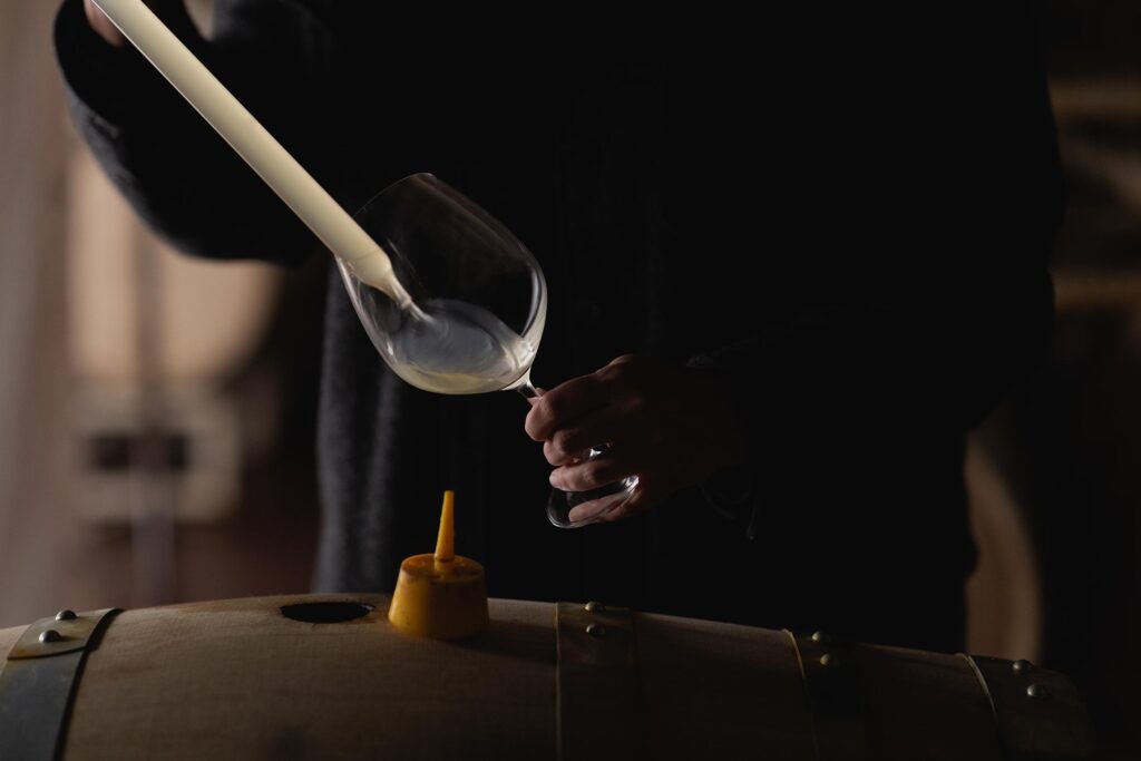 Winemaker Katie Vogt pours wine from a barrel into a glass using a wine thief.