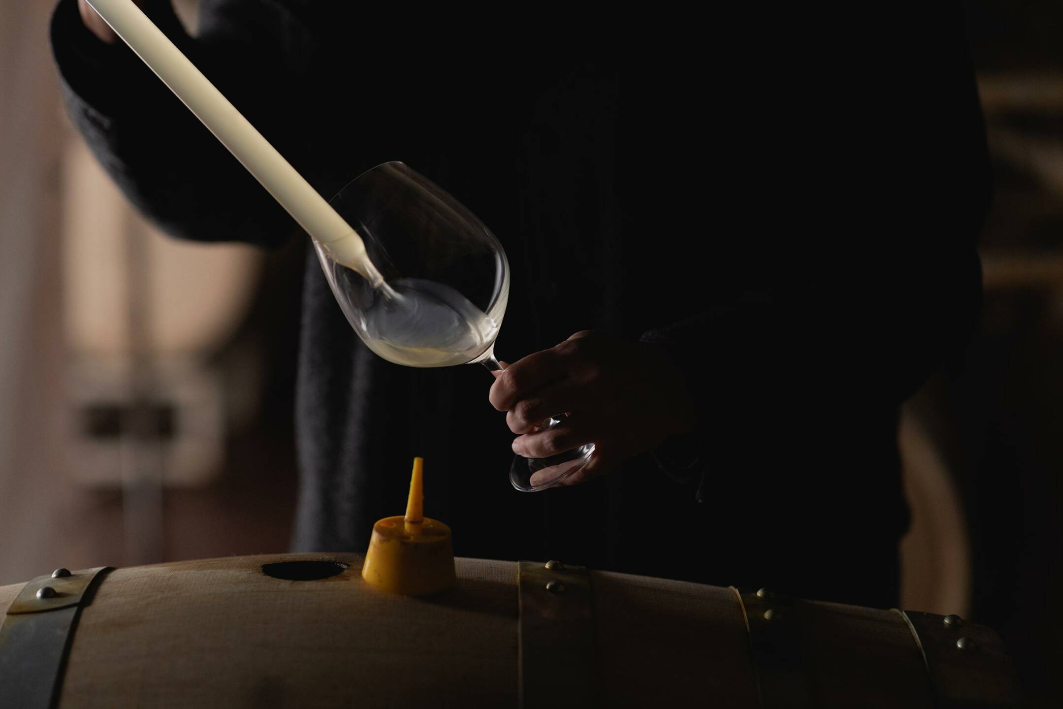 Winemaker Katie Vogt pours wine from a barrel into a glass using a wine thief.