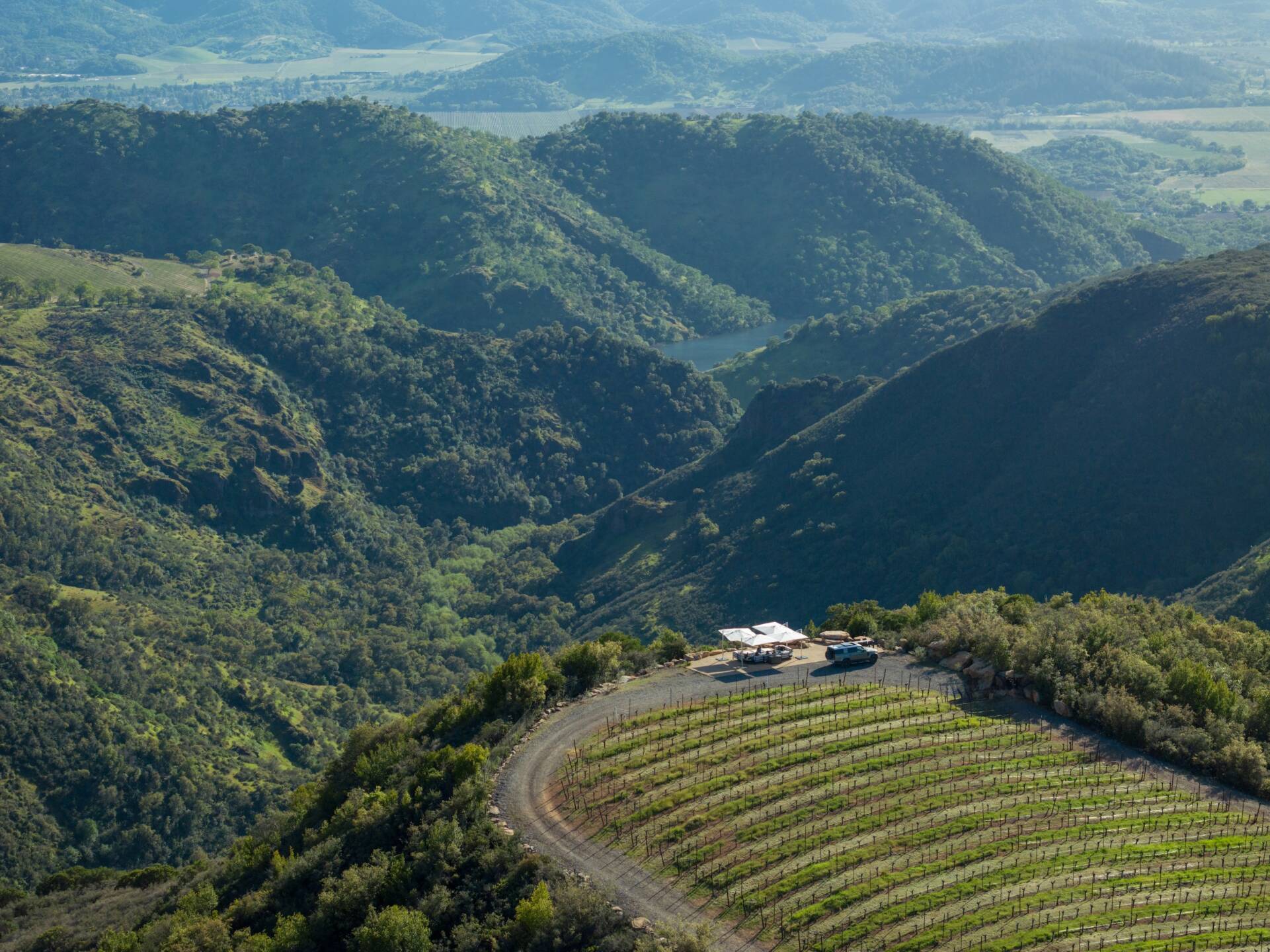 Aerial view of a secluded winery with a house and parked vehicle, located on a terraced hillside surrounded by lush, mountainous terrain.